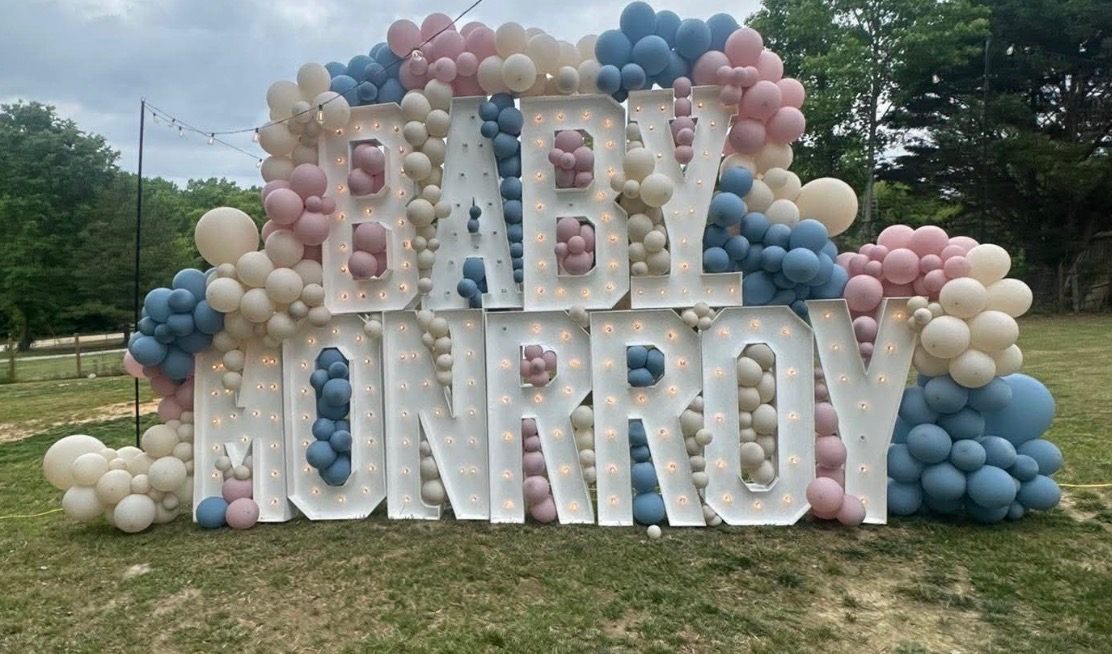 Gender reveal with giant light-up 'BABY MONRROY' marquee letters wrapped in pink and blue balloon garlands