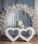 White floral arch over a double-heart sweetheart table with blue draping