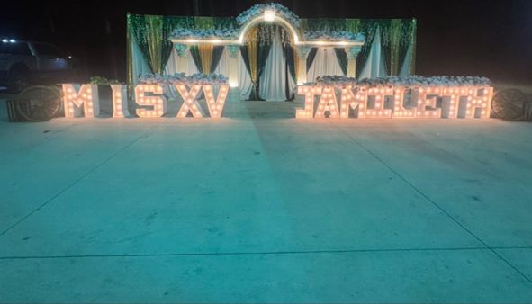 Outdoor quinceañera setup at night with 'MIS XV' light-up marquee letters and a draped floral entrance