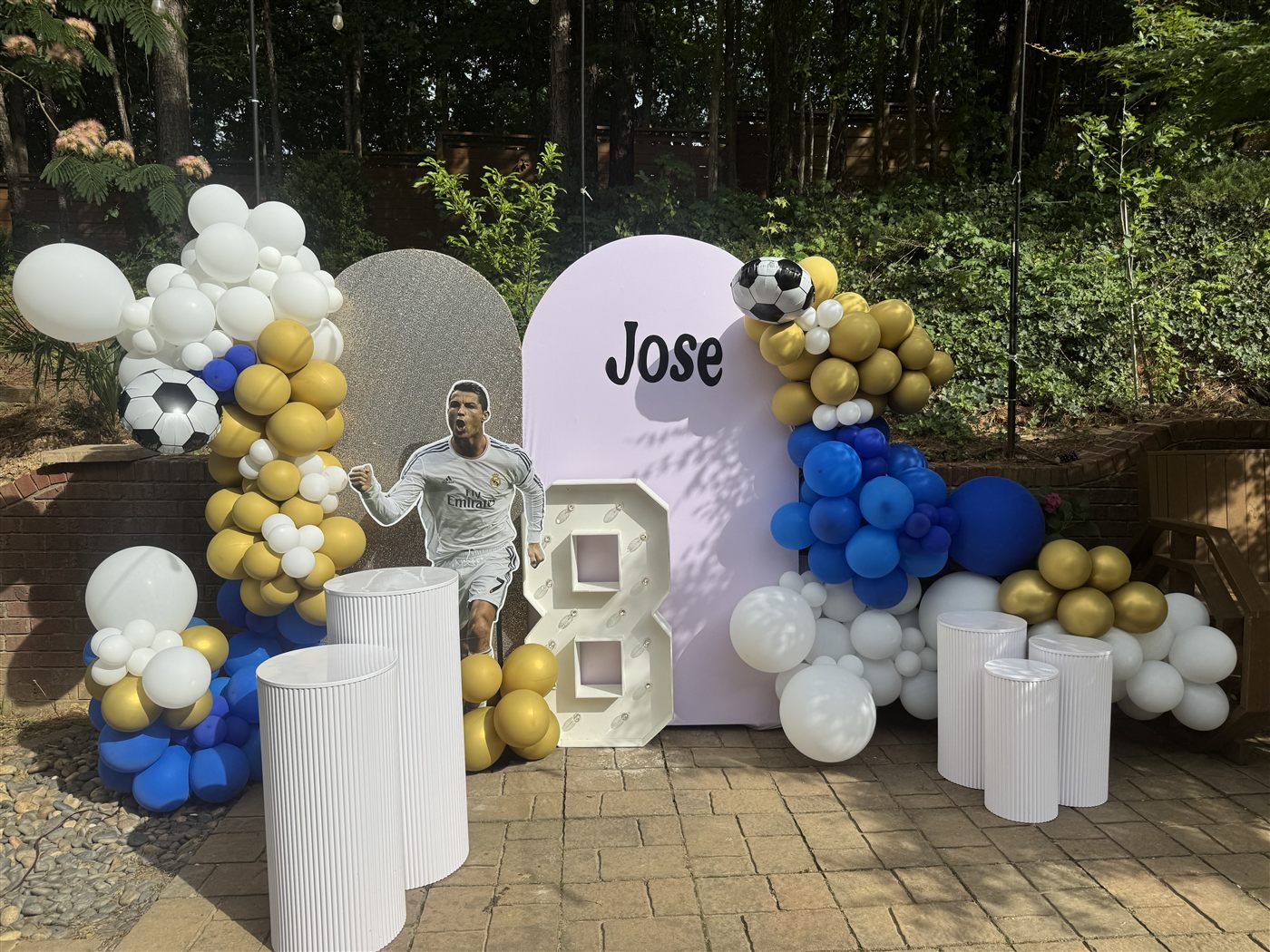 Soccer-themed birthday with blue, gold, and white balloon garlands, a Ronaldo cutout, a light-up 8, and a 'Jose' backdrop
